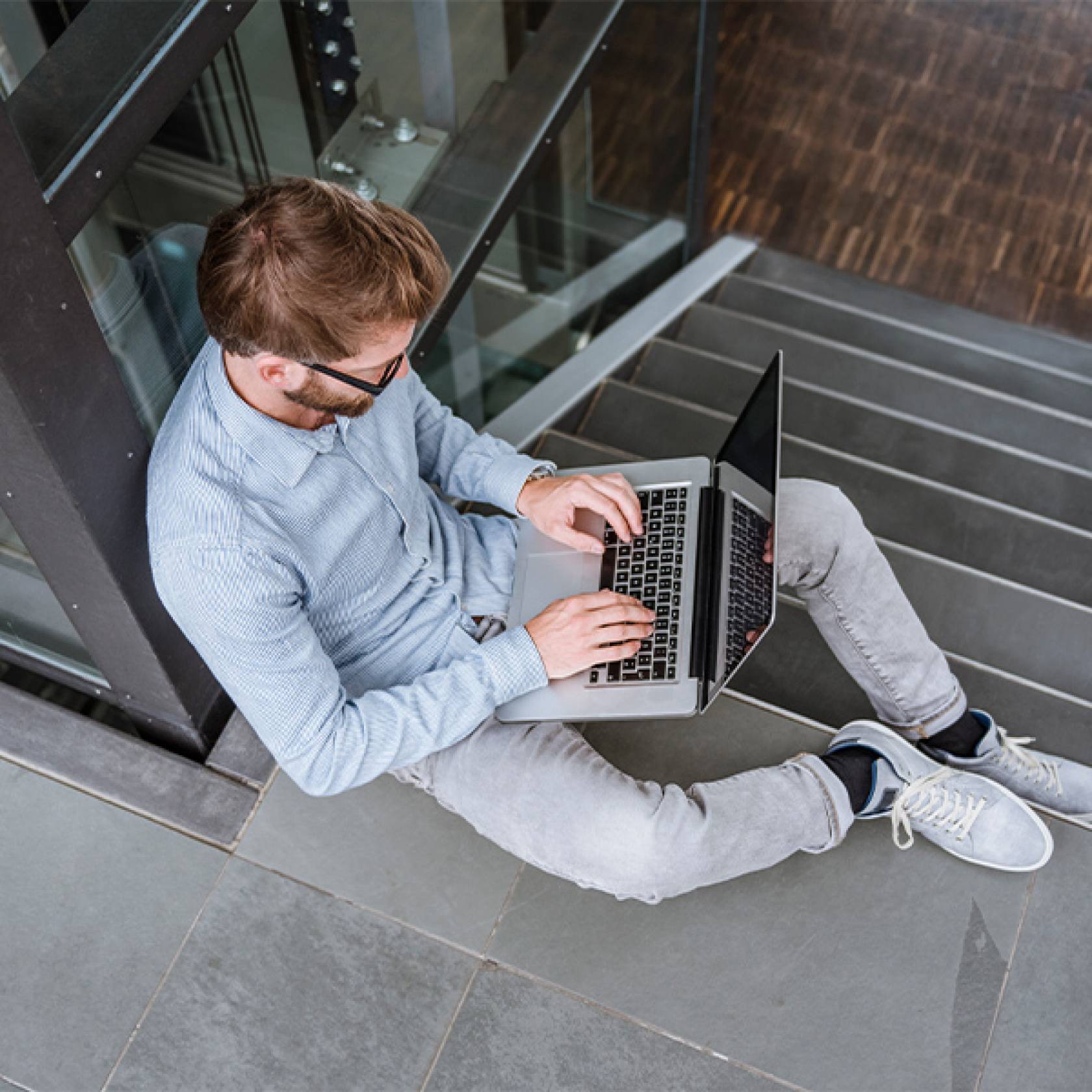 Wiki Schmuckbild 14 Ein Mann sitzt auf einer Treppe und arbeitet an einem Laptop